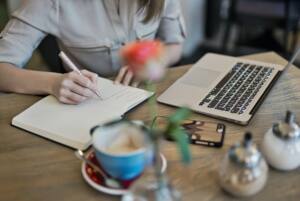 person-writing-on-a-notebook-beside-macbook-1766604